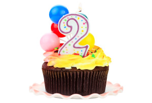 Chocolate birthday cake with number two candle and plastic balloons. Isolated on a white background.